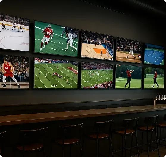 A row of TV screens above a bar shows various live sports including football, basketball, baseball, tennis, and golf; empty barstools line the counter.