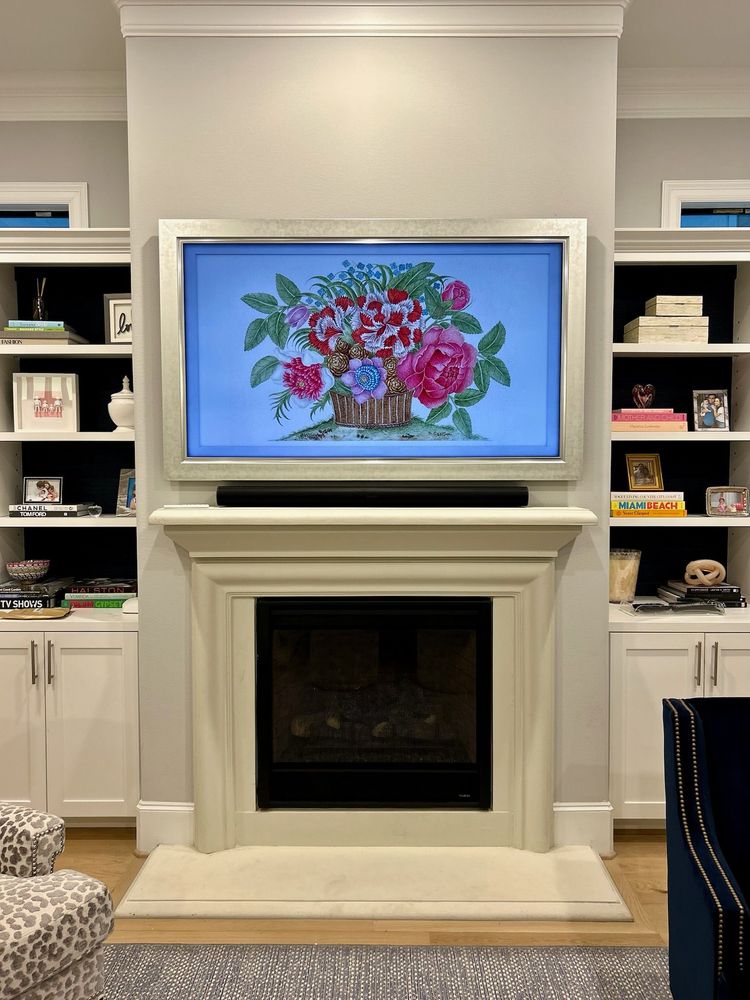 A fireplace with a mantel sits below a wall-mounted TV displaying a floral image, flanked by built-in shelves holding books, photos, and decorative items.