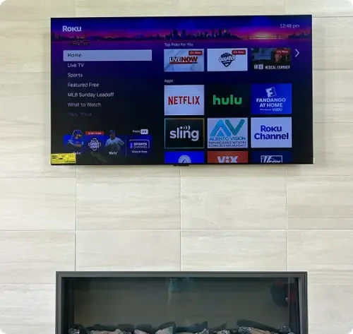 A wall-mounted TV displays the Roku home screen above a modern fireplace with a stone tile backdrop.