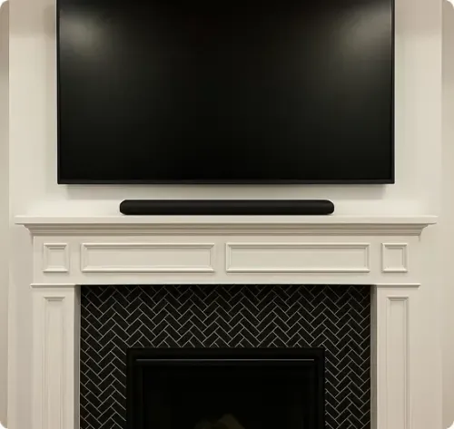 A flat-screen TV and soundbar are mounted above a white fireplace with a black herringbone tile pattern inside the opening.